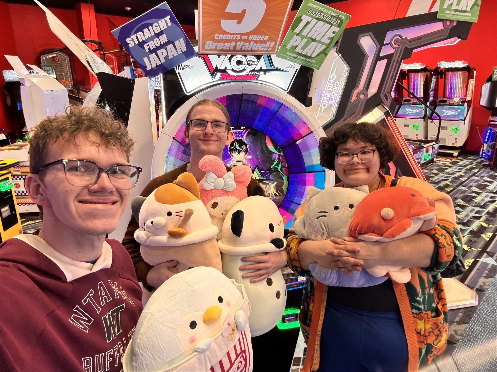 Three convention attendees holding plush toys at an arcade