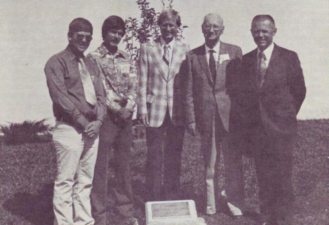 Five men standing behind the memorial plaque for Rick Wilborn on the lawn
